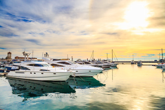 Fototapeta Luxury yachts at sunset. Marine dock of modern motor and sailing boats in sunshine, blue water sea, rainbow with sun. Travel and fashionable vacation.