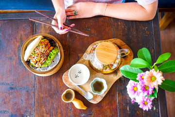 Grilled tuna and guacamole bao. Female hand with chopsticks. Wooden table background in a restaurant. Teapot of green Chinese tea. Traditional Chinese and French cuisine. Top view with copy space