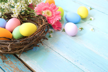 Colorful Easter eggs in nest with flowers on blue wooden background.  Easter holiday in spring season, top view with composition.