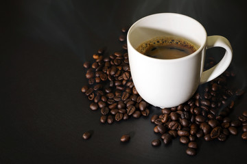 Hot coffee in white ceramic glass and coffee beans placed on the black table.