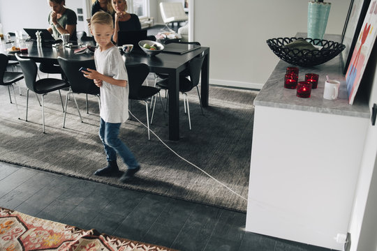 High angle view of boy pulling charging cable while family sitting at dining table