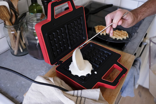 Cropped image of man pouring batter on waffle iron at kitchen counter