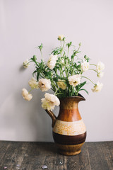 Very nice stylish clay pitcher wit a bunch of white ranunculus in it on the grey wall background