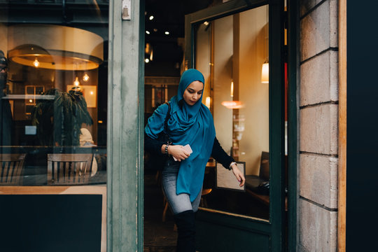 Young woman wearing hijab leaving store in city