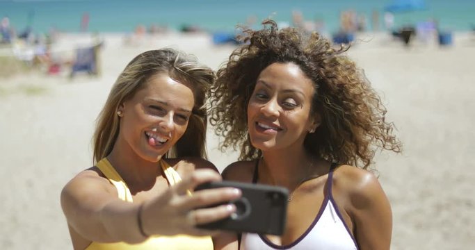 Confident diverse girls in sportswear looking confident while posing for selfie using phone on shoreline. 