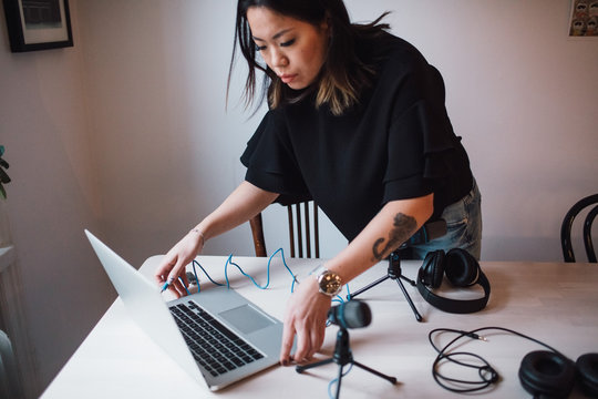 Female blogger using laptop standing by table with microphone at home