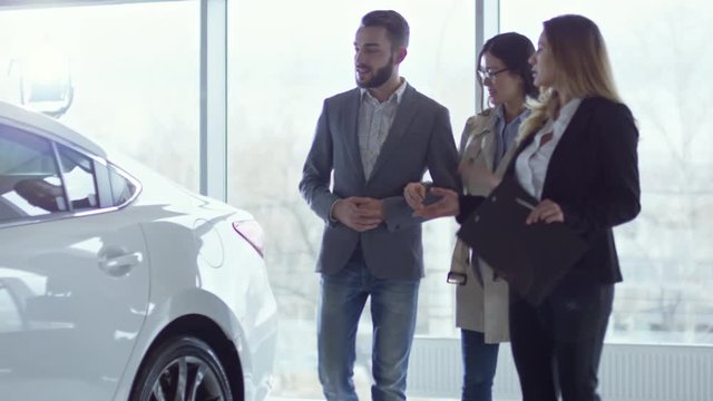 Tilt up of successful businessman and his wife talking with professional saleswoman while choosing new car in dealership
