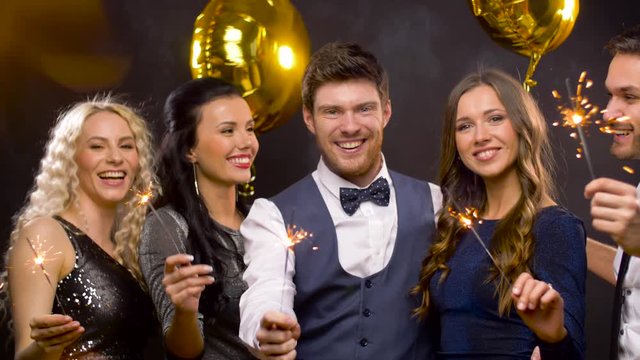celebration, people and holidays concept - happy friends at christmas or new year party with sparklers and golden balloons over black background