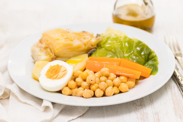 boiled cod fish with potato, carrot, cabbage , chick-pea and egg on white plate