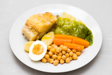 boiled cod fish with potato, carrot, cabbage , chick-pea and egg on white plate