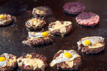 portions of beef meat with cheese and eggs grilling on stove