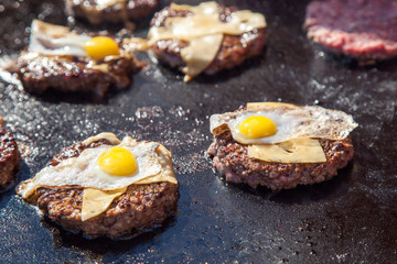 portions of beef meat with cheese and eggs grilling on stove