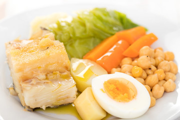 boiled cod fish with potato, carrot, cabbage , chick-pea and egg on white plate