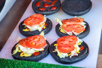 buns with tomatoes and cabbage with ketchup and mustard on white surface, preparation of black burgers concept