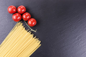 Yellow long raw spaghetti and cherry tomatoes on black slate plate