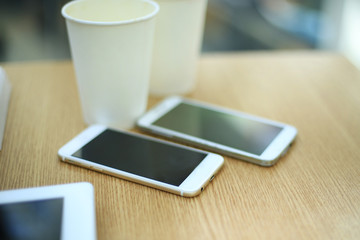 Two white mobile phones with tablet on wooden table background, blank screen electronic device with copy space.