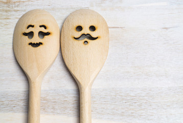 Wooden spoon with funny faces, woman and man, on wooden background