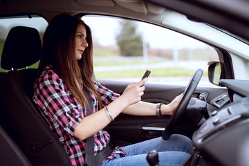 Young careless cute girl is texting and driving at same time.