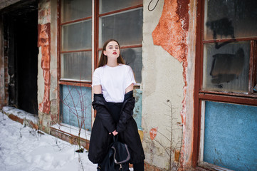 Fototapeta na wymiar Fashionable long legs brunette model in long black cloak posed outdoor at winter day against old grunge wall with broken windows.