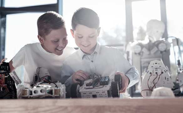 Supportive relations. Low angle shot of two extremely happy schoolboys smiling cheerfully while reuniting in a workshop and collaborating over their own moving robot.