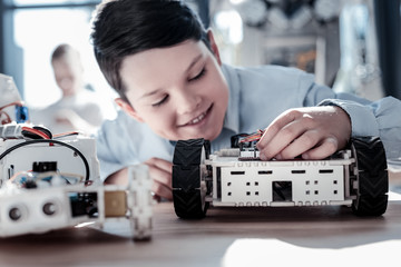 Up and coming schoolboy. Selective focus on a self driving robot standing on a table while a smart preteen kid smiling and adjusting it during a workshop session.