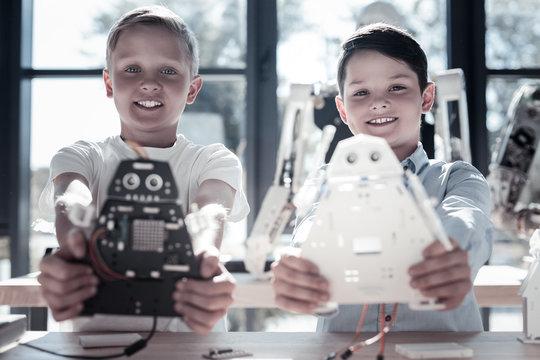 The work is done. Selective focus on positive minded youngster looking into the camera with cheerful smiles on their faces while holding their newly constructed robots.