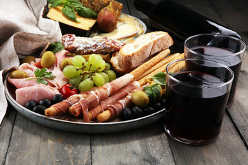 Italian antipasti wine snacks set. Cheese variety, Mediterranean olives, pickles, Prosciutto di Parma, salami and wine in glasses over black grunge background.