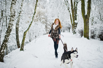 Red haired girl walking at park with husky dog on winter day.