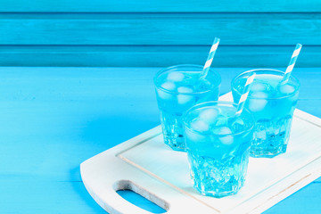 Blue cocktail with ice and mint in glasses on a white wooden board on a blue table.