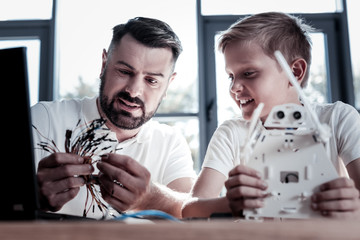 Two peas in a pod. Selective focus on a concentrated parent looking at wires while sitting next to his cheerful son and working on a new self automated robot together.