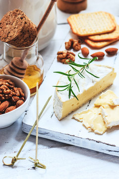 Cheese plate served with crackers, honey and nuts. Camembert on white wood serving board over white texture background. Appetizer theme.