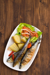 grilled sardines with boiled potato and salad on white plate