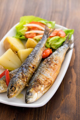 grilled sardines with boiled potato and salad on white plate