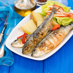 grilled sardines with boiled potato and salad on white plate