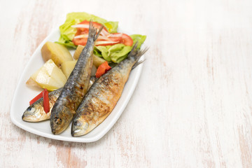 grilled sardines with boiled potato and salad on white plate