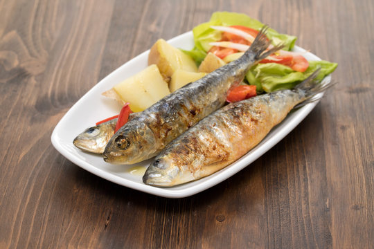 grilled sardines with boiled potato and salad on white plate
