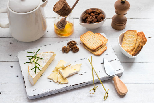 Cheese plate served with crackers, honey and nuts. Camembert on white wood serving board over white texture background. Appetizer theme. Top view