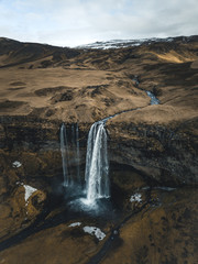 Aerial photograph of a waterfall dropping down a brown overgrown cliff at Seljalandsfoss, Iceland