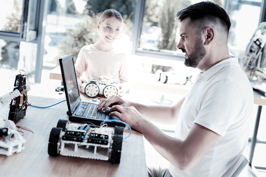 Help Is What Really Matters. Side View On A Focused Mature Man Sitting At A Laptop While Helping His Excited Female Student With Her Robotic Machine.