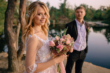 happy newlyweds standing against nature background at sunset