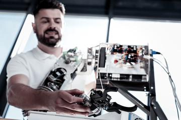 Finishing touches. Selective focus on a hand of a mature gentleman smiling while looking at his ne robot and constructing it in a workshop.