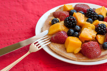 Pancake with fruit and berries in the plate on the red cloth