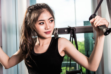 Young sporty girl working out on pull-down machine in gym