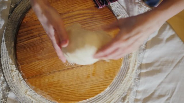 Top view: hands knead the dough on a wooden board. The board is oiled with vegetable oil