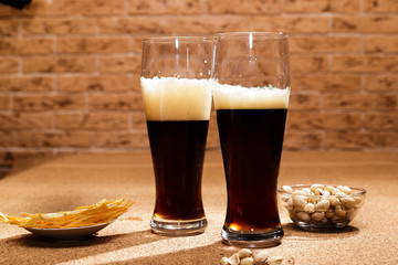 Two glasses of dark beer and a plate of snacks are on the table.