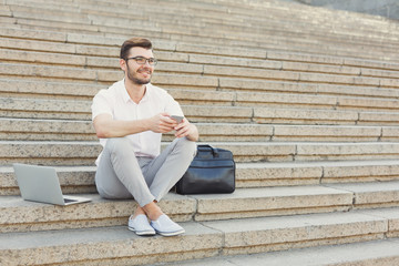 Cheerful young businessman messaging on cell phone sitting on st