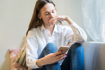 Crying young European woman in depression looking at phone gets bad news, covering mouth with hand,...