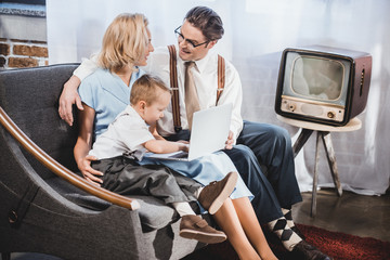happy 50s style family with one child using laptop together at home
