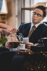 cropped shot of woman pouring coffee to husband reading newspaper, 1950s style