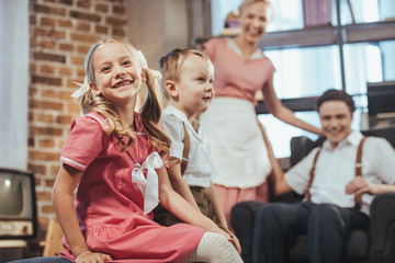 Fototapeta premium adorable happy kids sitting on foreground while happy parents smiling behind, 1950s style